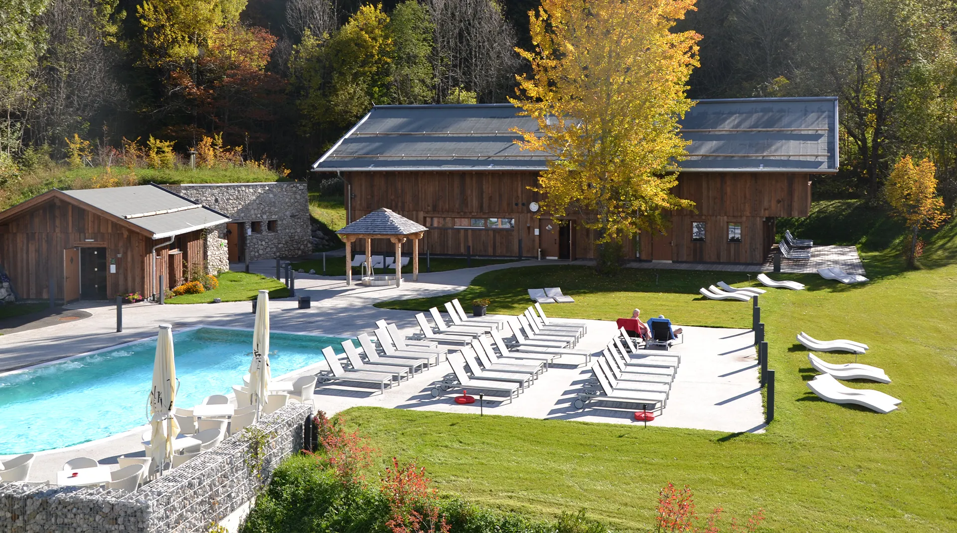 Schwimmbad mit Liegestühlen und grüner Landschaft  