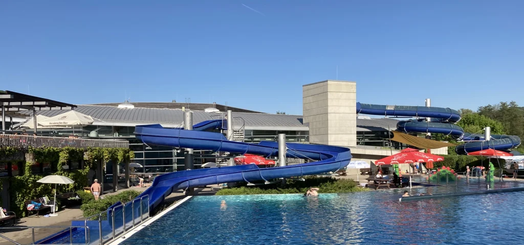Aussenbecken eines Schwimmbades mit Rutschen im Hintergrund